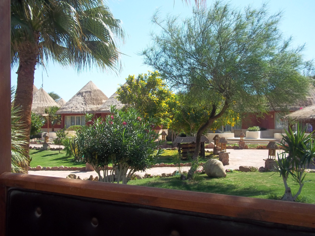 Eine Resort-Szene mit Hütten, Grünzeug, Felsen, einer Bank und Himmel.