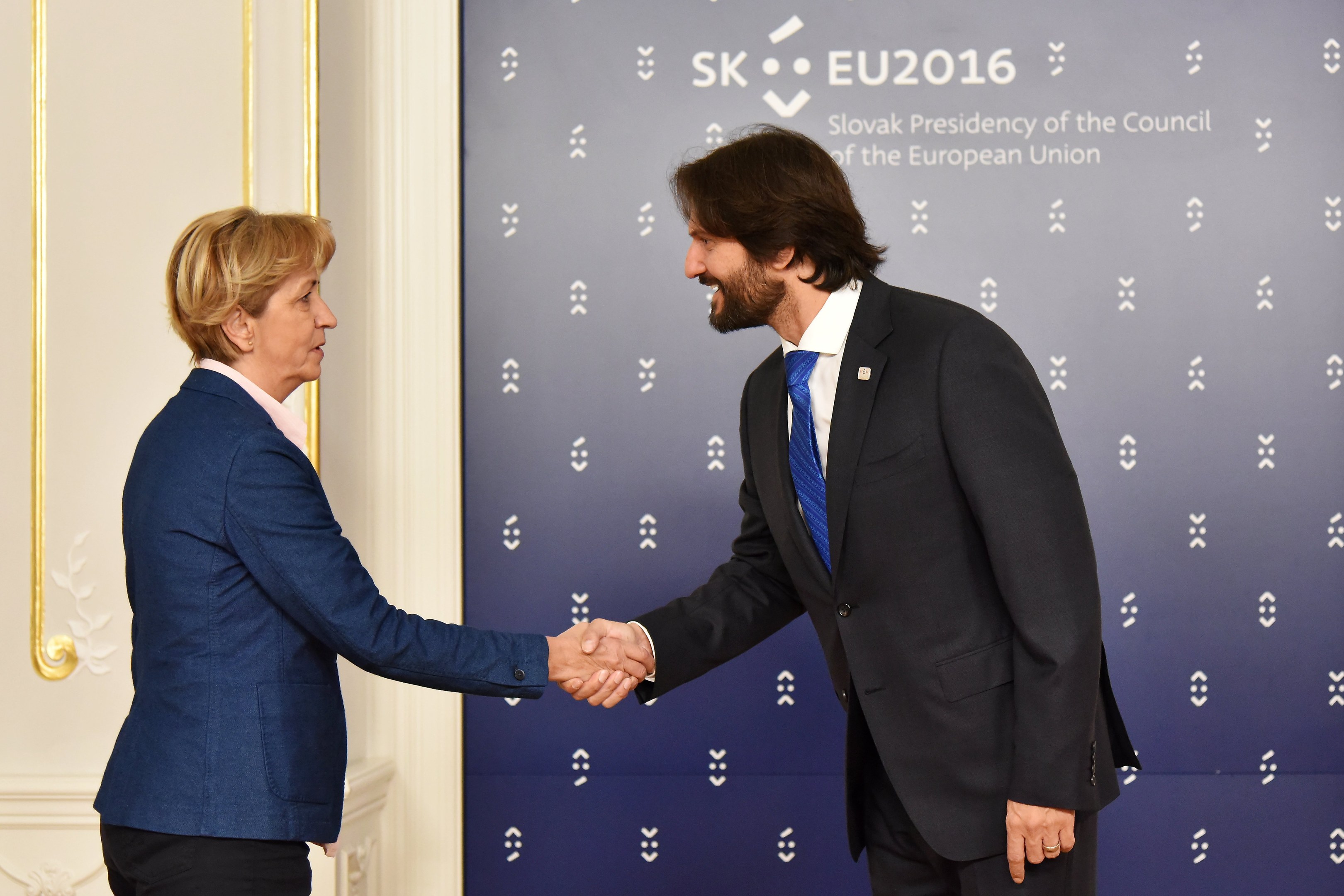 Bundeskanzlerin Angela Merkel und Bundespräsident Joachim Gauck schütteln sich die Hände vor einem 'EU-Gipfel'-Plakat und lächeln freundlich.