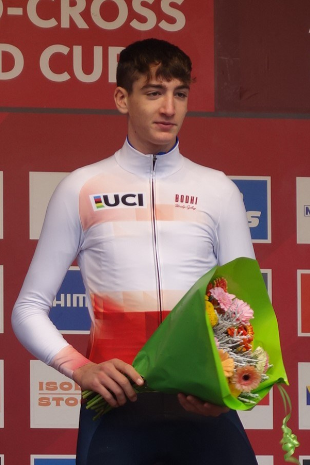 Ein Mann steht selbstbewusst auf einem Podium und hält einen Blumenstrauß, während er seinen Sieg feiert.