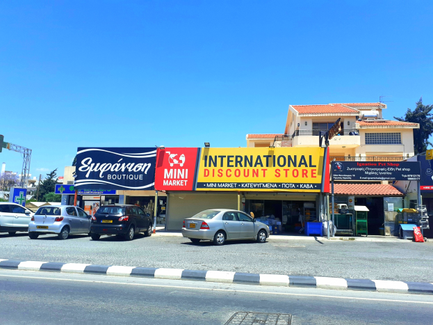 Internationaler Discounter an einer Straßenecke mit umliegenden Gebäuden, Fahrzeugen und städtischer Infrastruktur unter einem klaren blauen Himmel.