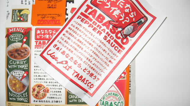 Ein Prospekt, das Pfeffersoße bewirbt, mit einem darunter liegenden Blatt, auf dem Werbung für verschiedene Currys zu sehen ist.