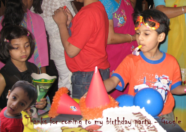 Kinder stehen vor einem Tisch mit einem Kuchen, Luftballons und Mützen, hinter ihnen stehen Erwachsene.