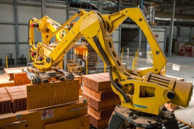 Großes industrielles Lagerhaus mit gestapelten Kisten, Überhead-Kränen, Zaun, Pfählen und einer fernen Wand in einer Fertigungsumgebung.