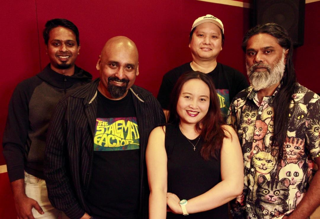 Eine Gruppe von Menschen, die zusammen in einem Aufnahmestudio posen, lächeln und leger gekleidet sind und ihre Arme umeinander legen.