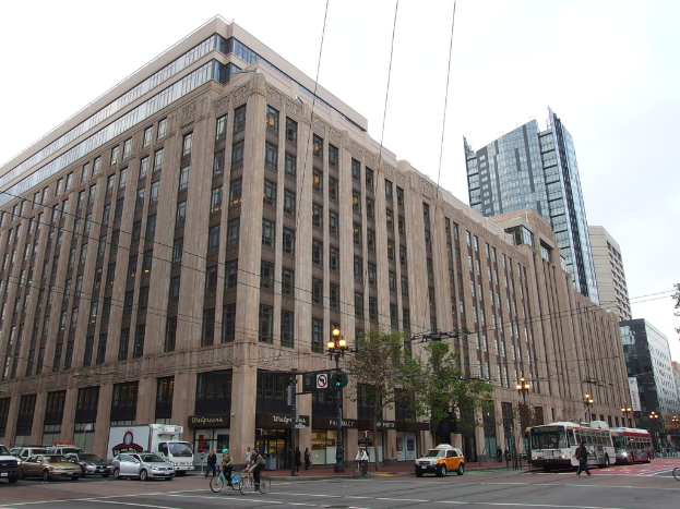 Eine Straße mit Menschen auf Fahrrädern, Bussen und Autos, mit Gebäuden, Bäumen, Lampen, Pfählen und Drähten im Hintergrund unter einem Himmel.