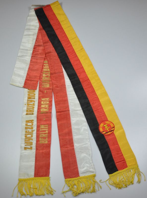 Ein roter, gelber und schwarzer gestreifter Schal mit dem Logo der deutschen Fußballnationalmannschaft darauf, der auf einer weißen Oberfläche liegt.