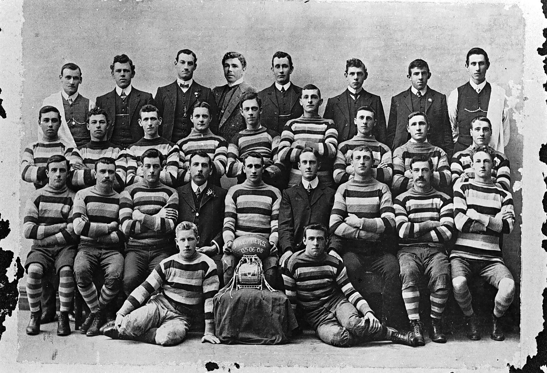 Schwarzes und weißes Foto einer Fußballmannschaft mit sitzenden und stehenden Spielern, einem Helm in der Mitte und einem unscharfen Hintergrund.