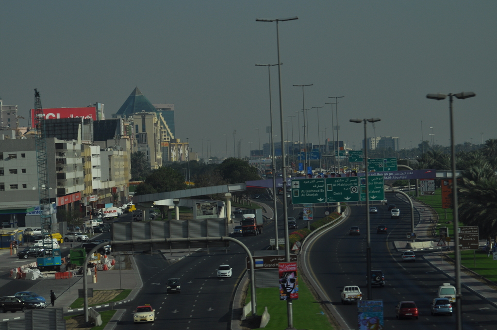 Eine Luftaufnahme einer Stadt mit Gebäuden, Türmen, Straßen, Fahrzeugen, Straßenlaternen, Bäumen, Menschen und verschiedenen Schildern und Werbetafeln.