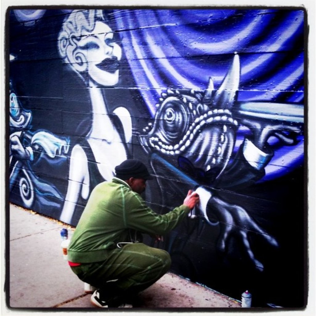Eine Person mit einer Flasche in der Hand steht auf einer Straße mit mehreren anderen Flaschen drumherum, im Hintergrund eine mit Graffiti bedeckte Wand.