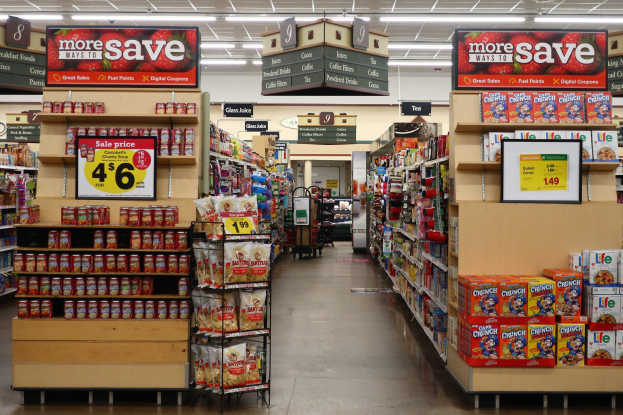 Ein Kiosk-Innenraum mit Regalen und Boden voller verschiedener Lebensmittel, Deckenbeleuchtung und einer nummerierten Tafel.