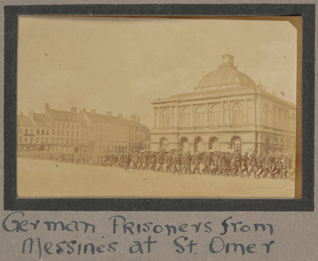 Gruppe deutscher Gefangener aus Messines vor einem Gebäude mit einem klaren blauen Himmel im Hintergrund, mit Text am unteren Bildrand.