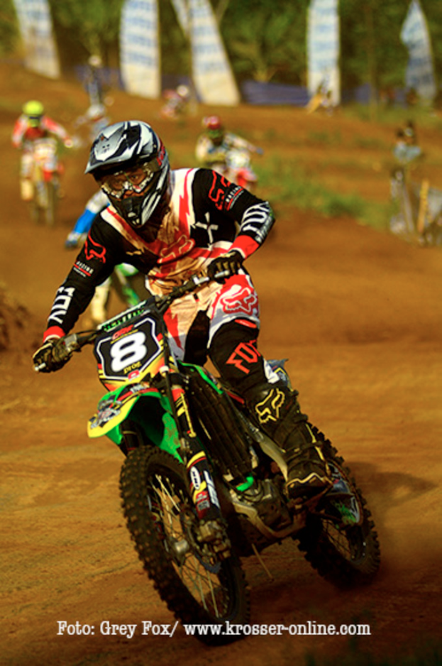 Mehrere Personen bei Motorradrennen, alle mit Helmen, mit Text am unteren Bildrand.