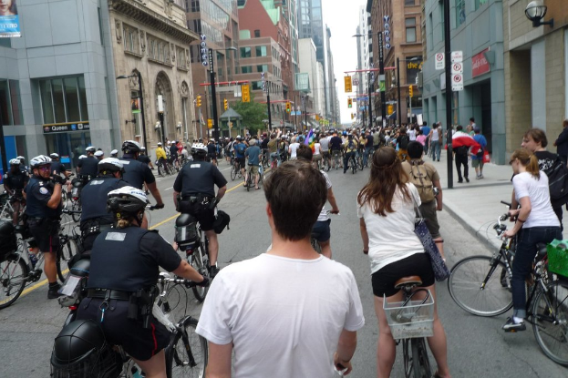 Gebäude säumen eine Straße, auf der ein paar Menschen Fahrrad fahren.