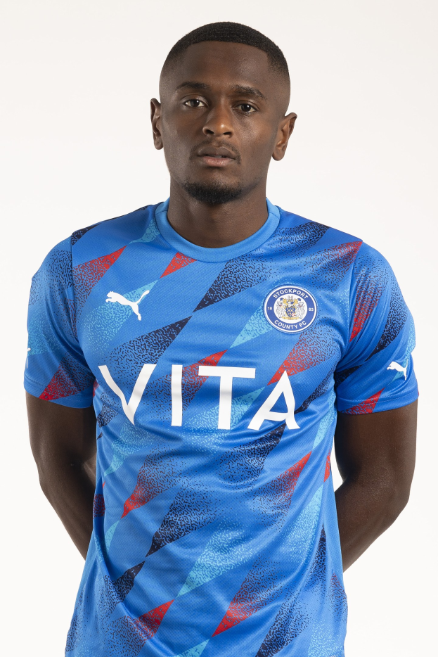 Ein Mann in einem blauen Leicester City Away-Shirt von der Saison 2018-19, der mit Händen in den Taschen und einem leichten Lächeln dasteht.