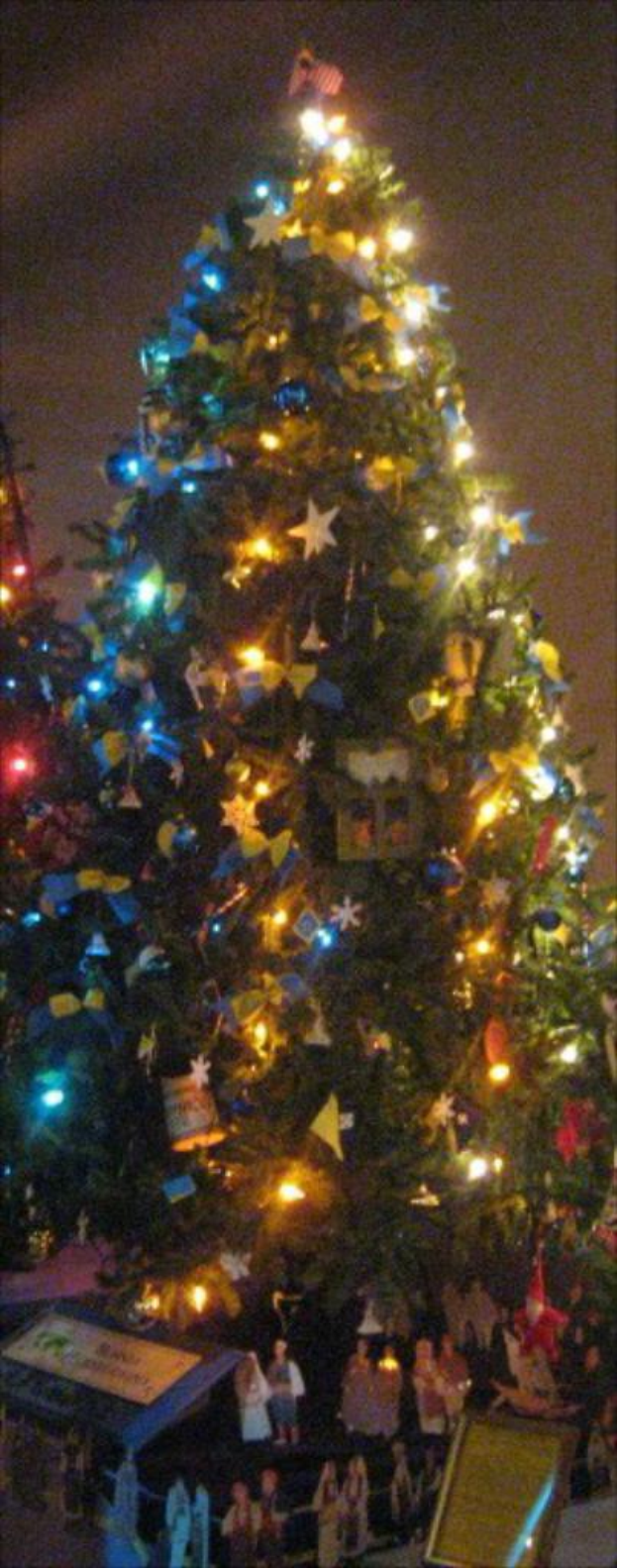 Ein geschmückter Weihnachtsbaum mit Menschenfiguren, die auf einem Tisch darunter platziert sind.