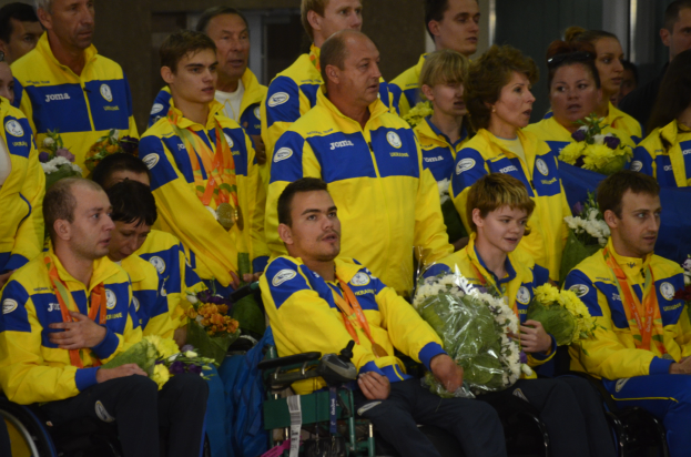 Eine Gruppe von Menschen im Rollstuhl, einige mit Blumensträußen und Medaillen, vor einer Wand.