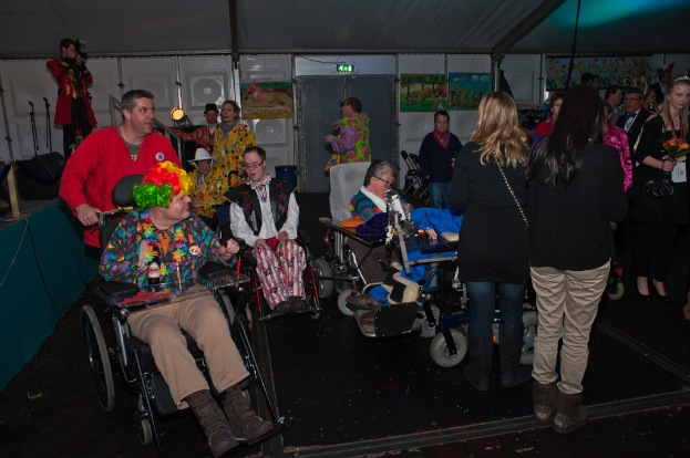 Menschen im Rollstuhl mit Kostümen, mit einer Menge im Hintergrund, die Gegenstände hält, unter einem Dach mit Lichtern, Rahmen, Brettern, Stangen und einem Tuch.