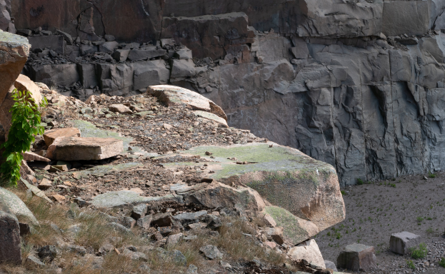 Ein steiniger Hügel mit einer markanten Felsformation in der Mitte, umgeben von Gras und kleinen Pflanzen.