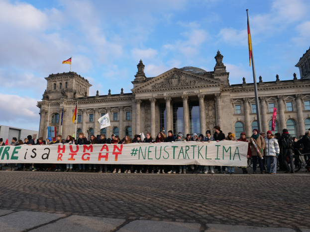 Gruppe von Menschen, die ein Transparent mit der Aufschrift 'Wir sind ein Menschenrecht' vor dem Reichstaggebäude in Berlin, Deutschland, halten.