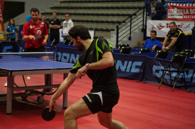 Eine Gruppe von Menschen in verschiedenen Farben, darunter schwarz, weiß und blau, sitzt um einen Tisch mit einem Spiel im Hintergrund, Stühle und eine Treppe.