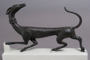 Eine Bronzestatuette eines Greyhounds auf einem weißen Sockel vor einem grauen Hintergrund mit detaillierten Einzelheiten des Fells und der Merkmale des Hundes.